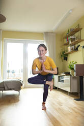 Smiling young woman with hands clasped exercising at home - MIKF00386