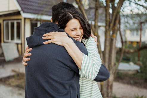 Happy couple embracing in front yard with house in background - ANAF01425