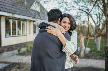 Glückliche Frau umarmt Mann am Haus - ANAF01426