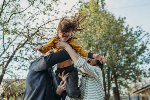 Playful parents lifting son in front yard - ANAF01436