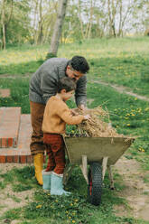 Vater und Sohn legen Heu in eine Schubkarre im Hinterhof - VSNF00890