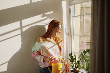 Redhead woman watering plants on window sill at home - MDOF01109