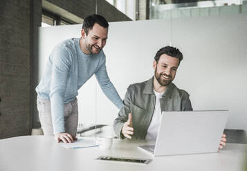 Lächelnde Geschäftskollegen, die über einem Laptop im Büro diskutieren - UUF28560