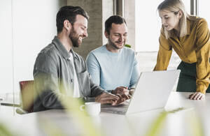 Lächelnde Geschäftskollegen bei der Arbeit am Laptop im Büro - UUF28568