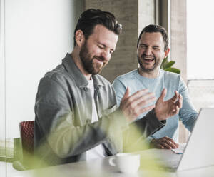 Businessman laughing with colleague at office - UUF28571