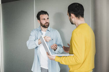 Businessman explaining colleague holding laptop at office - UUF28573