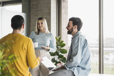 Young businesswoman with coffee cup discussing with colleagues at office - UUF28583