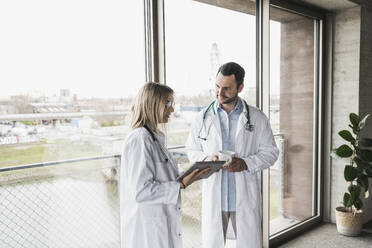 Arzt schaut auf einen Kollegen, der einen Tablet-PC im Krankenhaus benutzt - UUF28595