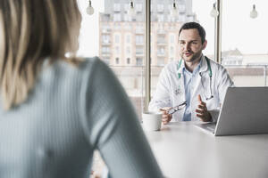 Arzt konsultiert Patientin am Tisch sitzend in der Klinik - UUF28604