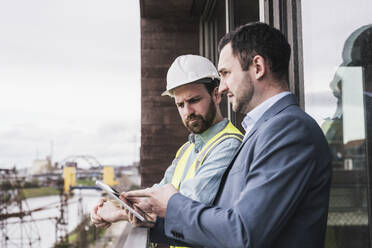 Architect explaining building contractor over tablet PC by railing - UUF28612