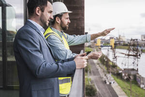 Bauunternehmer gestikuliert vor einem auf dem Balkon stehenden Architekten - UUF28613