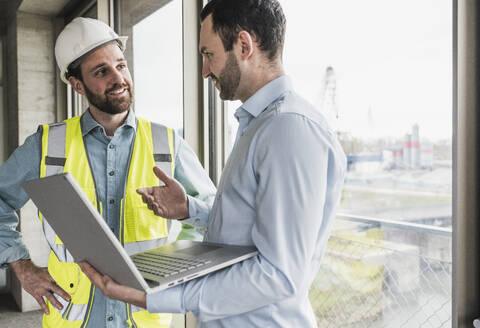 Architect holding laptop discussing with building contractor at site - UUF28616