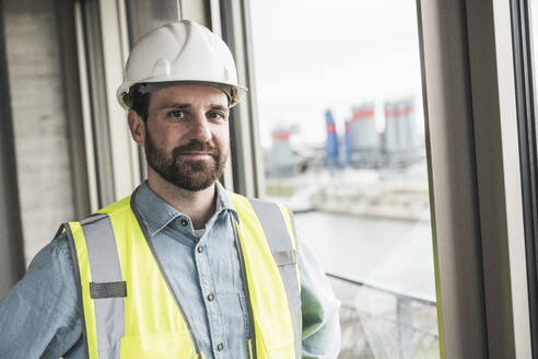 Smiling building contractor wearing hardhat at site - UUF28620