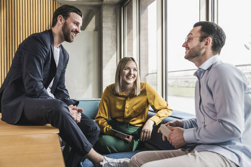 Happy business colleagues sitting on couch at workplace - UUF28628