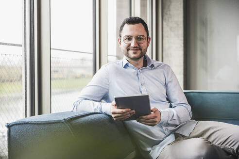 Lächelnder Geschäftsmann mit Tablet-PC auf der Couch im Büro - UUF28639