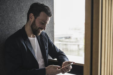 Lächelnder Geschäftsmann mit Smartphone im Büro - UUF28642