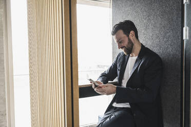 Lächelnder Geschäftsmann, der über sein Smartphone im Büro Textnachrichten verschickt - UUF28643