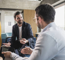 Smiling businessman and colleague discussing at workplace - UUF28648