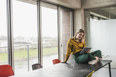 Young businesswoman using tablet PC sitting on table at workplace - UUF28659