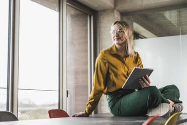 Contemplative businesswoman with tablet PC sitting on table at office - UUF28660