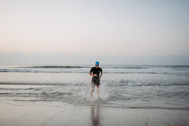 Woman in a neoprene running out of the ocean. - HPIF09653