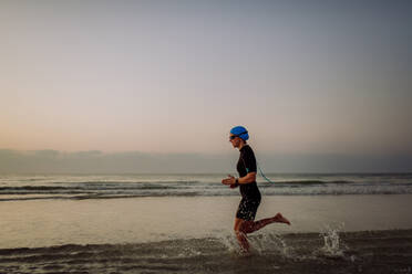 Side view of young woman in neoprene running in ocean. - HPIF09655