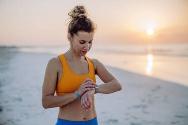 Young woman taking exercises at beach and checking the smartwatch, morning routine and healthy lifestyle concept. - HPIF09667