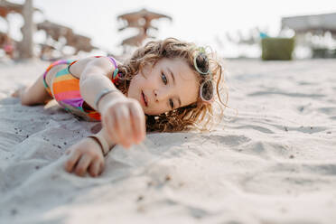 Little girl playing on the beach, lying in sand. - HPIF09684