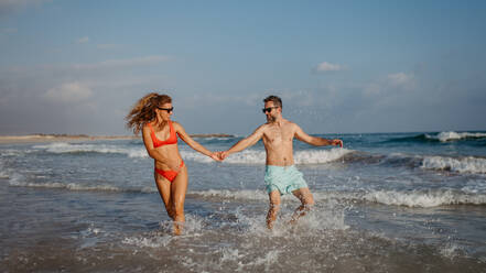 Happy couple enjoying time in sea during vacation, running, having fun. - HPIF09699