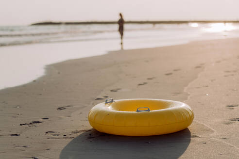 Nahaufnahme eines gelben aufblasbaren Rades am Strand, mit einer Person im Hintergrund. - HPIF09705