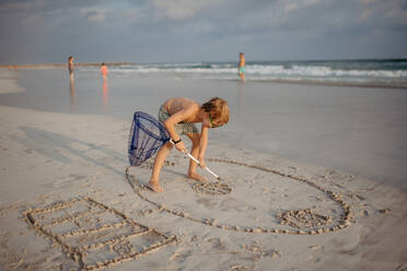 Little boy playing and drawing in a sand with a fishing net, enjoying holiday time. - HPIF09706