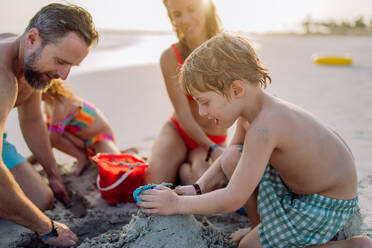 Glückliche Familie mit kleinen Kindern, die die Zeit am Meer in einem exotischen Land genießen und eine Sandburg bauen. - HPIF09708