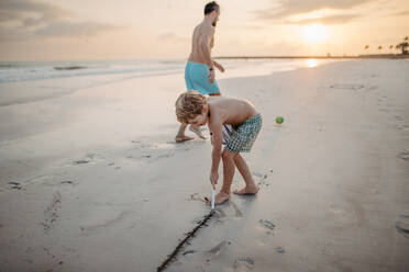 Kleiner Junge, der mit einem Fischernetz im Sand spielt und zeichnet, bereitet sich mit seinem Vater auf ein Fußballspiel vor. - HPIF09718