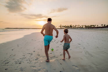 Rückansicht eines Vaters mit seinem Sohn, der an einem Strand Fußball spielt. - HPIF09720