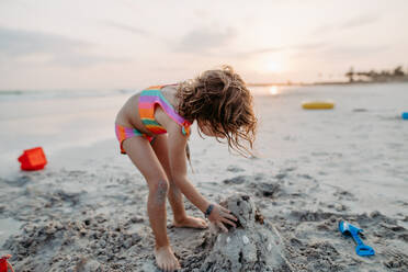 Kleines Mädchen spielt am Strand und baut eine Sandburg. - HPIF09723