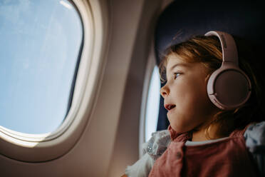 Kleines Mädchen im Flugzeug, das Musik hört und aus dem Fenster schaut. - HPIF09767