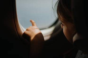 Kleines Mädchen im Flugzeug, das Musik hört und aus dem Fenster schaut. - HPIF09768