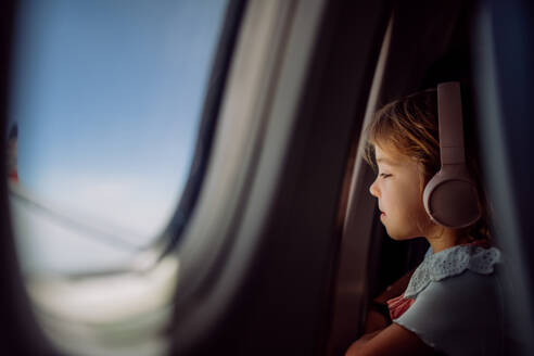Kleines Mädchen im Flugzeug, das Musik hört und aus dem Fenster schaut. - HPIF09769