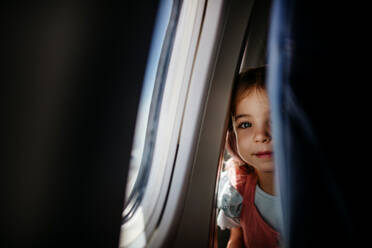 Little curious girl looking through seat in the airplane. - HPIF09770