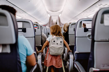 Rear view of little girl with backpack standing in aisle in the plane. - HPIF09773