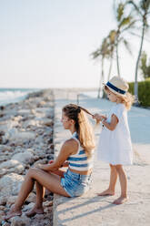 Kleines Mädchen macht Frisur ihre Mutter, genießen Sommerzeit am Meer. - HPIF09786