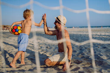 Father with his son plaing football on a beach. - HPIF09799
