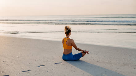 Rückansicht einer jungen Frau, die am Strand Übungen macht, Morgenroutine und gesundes Lebenskonzept. - HPIF09831