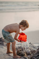 Kleiner Junge im Badeanzug spielt mit Eimer in der Nähe des Meeres und genießt den Sommerurlaub. - HPIF09844