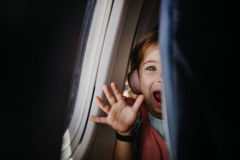 Kleines neugieriges Mädchen schaut durch den Sitz im Flugzeug. - HPIF09864