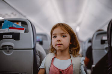 Smiling little girl with backpack standing in aisle in the plane. - HPIF09866