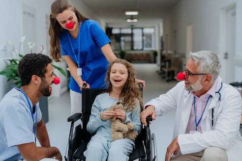 Glückliche Ärzte mit roten Clownsnasen, die sich um ein kleines Mädchen kümmern. - HPIF09916