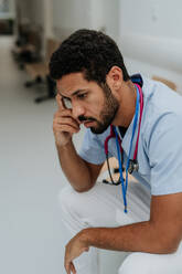 Blick von oben auf einen müden Arzt, der in einem Krankenhauskorridor sitzt. - HPIF09949