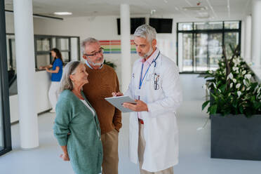 Mature doctor talking with his senior patients at hospital corridor. - HPIF09960