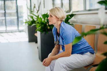 Young pensive doctor sitting at a hospital corridor. - HPIF09995